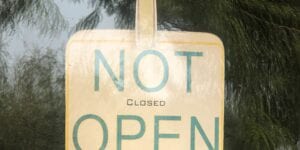 A sign in a window reads, "NOT OPEN" in large letters, in small letters in between it reads, CLOSED