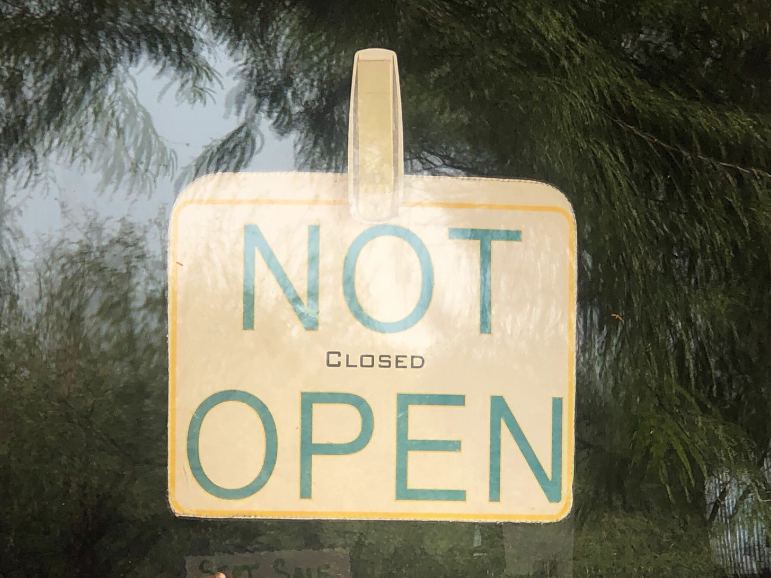 A sign in a window reads, "NOT OPEN" in large letters, in small letters in between it reads, CLOSED